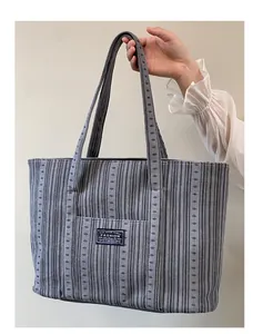 Detail of grey corduroy tote bag featuring a black fashion label and soft texture
