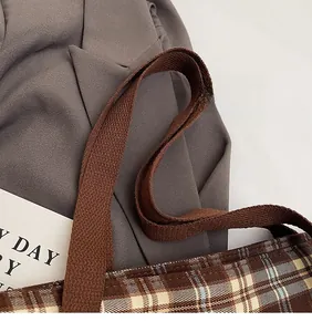 Détail d'un sac cabas à carreaux marron avec une bandoulière tissée épaisse sur tissu gris