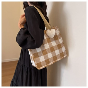 Brown and white plaid tote bag with a white plush heart charm on a woven shoulder strap