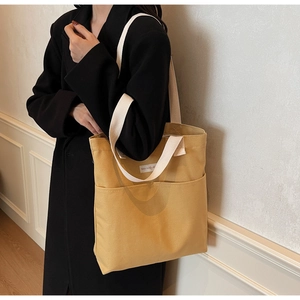 Detail of yellow canvas tote bag with off-white shoulder straps and exterior pocket