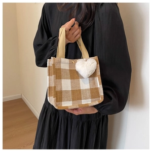 Detailed shot of the checkered tote bag featuring a white heart pom-pom charm and metal snap