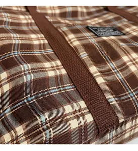 Détail du sac cabas à carreaux avec poignées marron robustes et écusson tissé de logo