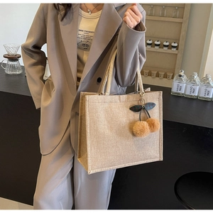 Detail shot of beige linen tote bag with plush cherry charm in a cafe setting