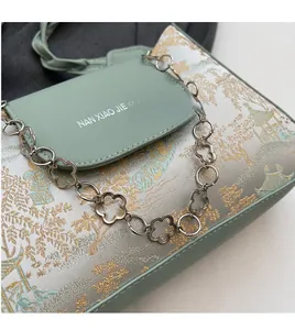 Detail of light green bag featuring plum blossom metal chain and landscape embroidery