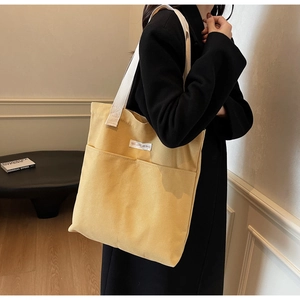 Detail view of a yellow canvas tote bag with front pockets and sturdy shoulder straps