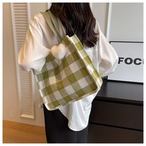 Detail of green and white plaid tote bag featuring a plush heart charm and woven strap