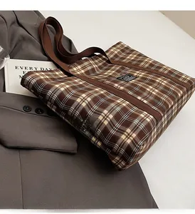 Gros plan d'un sac cabas en toile à carreaux marron posé sur une veste grise