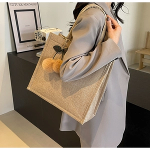 Close-up of khaki linen tote bag with plush cherry pendant worn over the shoulder