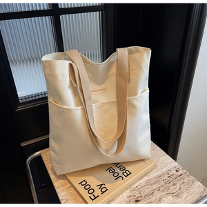 Detail of canvas tote bag showing khaki straps and front pockets on stone surface