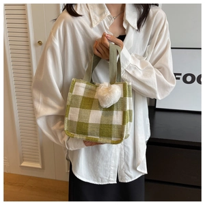 Close-up of green checkered tote bag featuring a cute white plush heart charm accessory