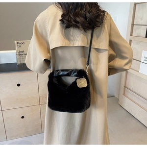 Detailed view of black faux fur shoulder bag with leather handle and gold tag logo