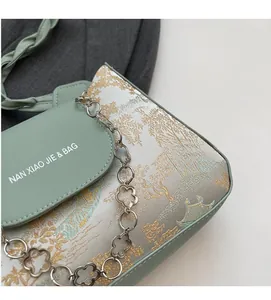 Detail of mint green baguette bag featuring traditional embroidery and a floral gold chain