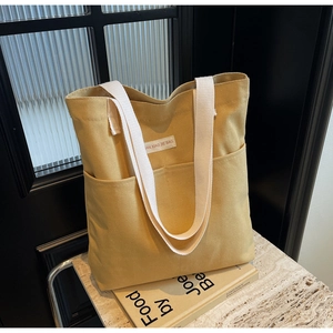 Detailed view of the yellow canvas tote bag with dual front pockets and woven straps
