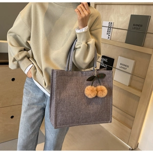 Detail of grey-purple linen tote bag featuring a plush cherry charm and thick woven texture