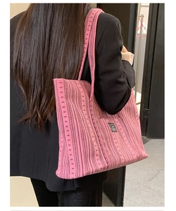 Detail of pink knitted tote bag featuring black stripes and pocket worn by a model