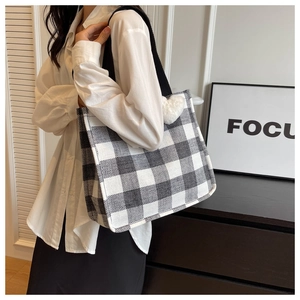 Detail of checkered tote bag with plush heart charm shown on model in modern setting