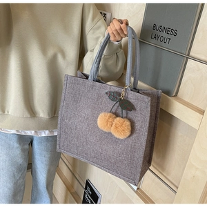 Detail of grey woven tote bag featuring a cute plush cherry charm and sleek top handles