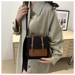 Close-up of a two-tone crossbody bag with black fabric and brown leather straps worn by a model