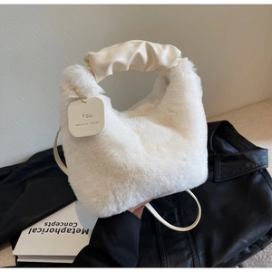 Close-up of plush white handbag featuring a pleated faux leather handle and charm