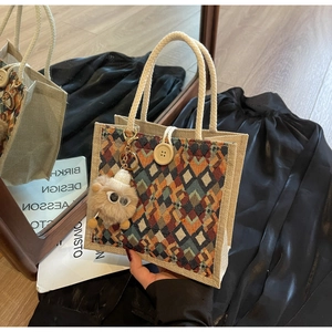 Detail of linen tote bag with geometric pattern, braided handles, and plush charm
