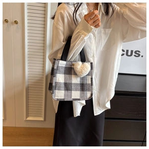 Detail of checkered tote bag with a white plush heart pendant on the black handle