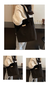 Detail of a large black canvas tote bag featuring a spacious front pocket and woven label