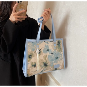 Détail du sac cabas en toile à fleurs bleues avec pompon et bandoulières en simili cuir