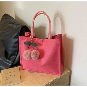 Pink canvas tote bag with woven texture and cherry pompom charm on a stone stand