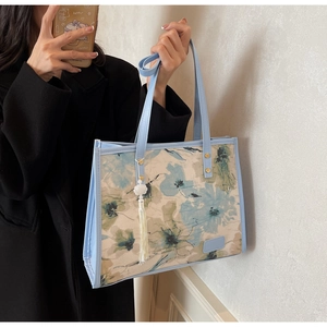 Détail du sac cabas floral avec lanières en cuir bleu et breloque à pompon