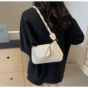 Detail of beige baguette bag with floral embroidery and decorative silver chain strap