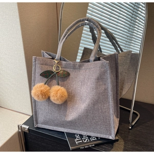 Detail of grey linen tote bag with fabric texture and cherry plush charm accessory