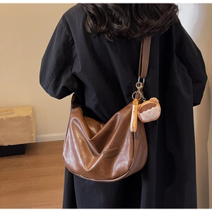 Detail of a large brown leather crossbody bag with a fashion logo and doll charm