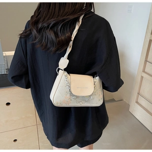 Detail of floral cream baguette bag with woven strap shown on a person back view