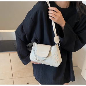 Detail of off-white baguette bag with floral prints and metallic chain held by model