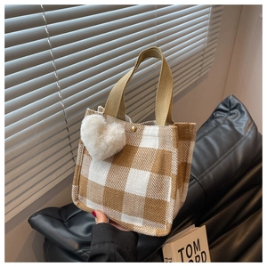 Detail of checkered tote bag with plush heart charm and woven strap for fall fashion