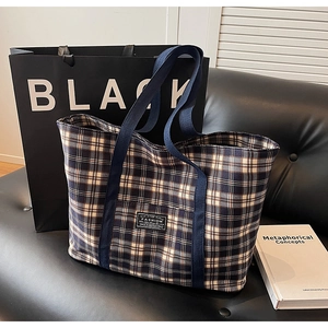 Détail d'un grand sac cabas à carreaux avec anses bleu marine et étiquette sur un canapé