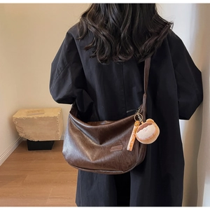 Detail of a deep brown hobo bag with vintage texture and a cute plush bear charm