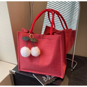 Detailed macro view of the red linen fabric texture and plush cherry charm on the tote bag
