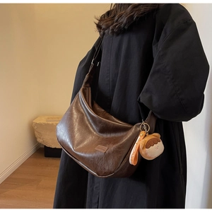 Detail view of dark brown crescent bag with a cute bear charm and fashion label