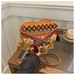Detail of colorful woven heart-shaped crossbody bag with tassels and leather strap