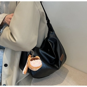 Detail of black pebbled leather Hobo bag featuring a side logo and cute cartoon plush pendant