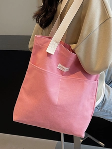 Pink canvas tote bag with front pockets and white shoulder straps worn by a model