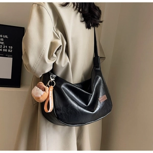 Close-up of black PU leather dumpling bag with FASHION label and plush doll charm
