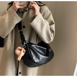 Detail of black leather hobo bag with adjustable strap and cute brown plush bear charm