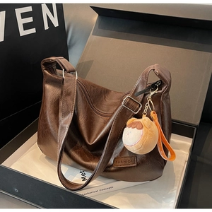 Detail of retro dark brown lychee texture bag with fashion label and plush doll charm