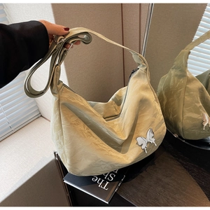 Détail du sac hobo plissé vert sauge avec un papillon argenté et une bandoulière large