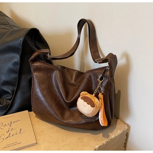 Detailed macro of dark brown leather hobo bag with fashion label and bear pendant