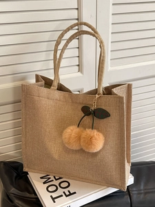 Large linen tote bag with cherry charm accessory on books by a white blind background
