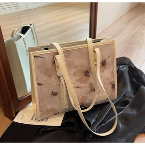 Détail d'un sac cabas en toile beige avec motifs floraux marrons et breloque à pompon