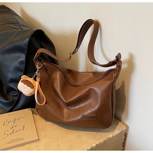 Close-up of brown textured leather bag with cartoon pendant and FASHION label detail
